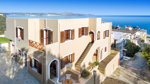 A Mediterranean-style building with multiple balconies, a courtyard with a table and chairs, and a view of the sea. - Avra Apartments (Apokoronas)