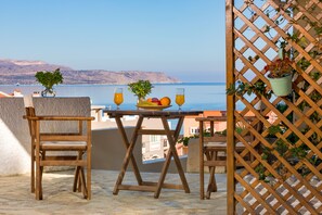 A wooden table with a fruit bowl and two glasses of orange juice, set on a balcony overlooking the sea. - Avra Apartments (Apokoronas)