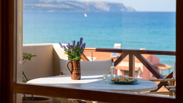 A balcony with a table, a potted plant, and a view of the sea. - Avra Apartments (Apokoronas)