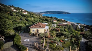 A coastal villa with a terracotta roof, surrounded by lush greenery and a clear view of the sea.