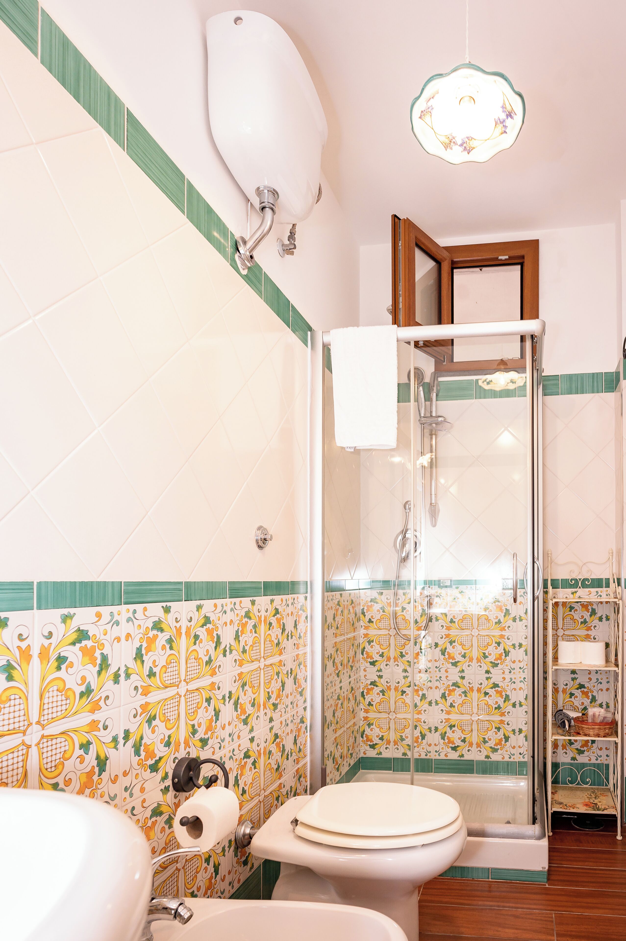 A bathroom with a shower, toilet, and sink, featuring patterned tiles and a hanging light fixture.