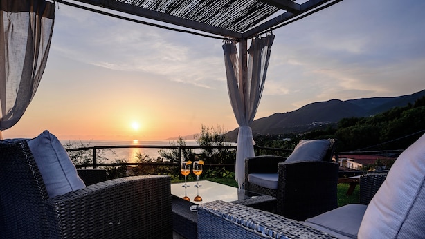 An outdoor seating area with wicker furniture and a table, overlooking a scenic sunset view.