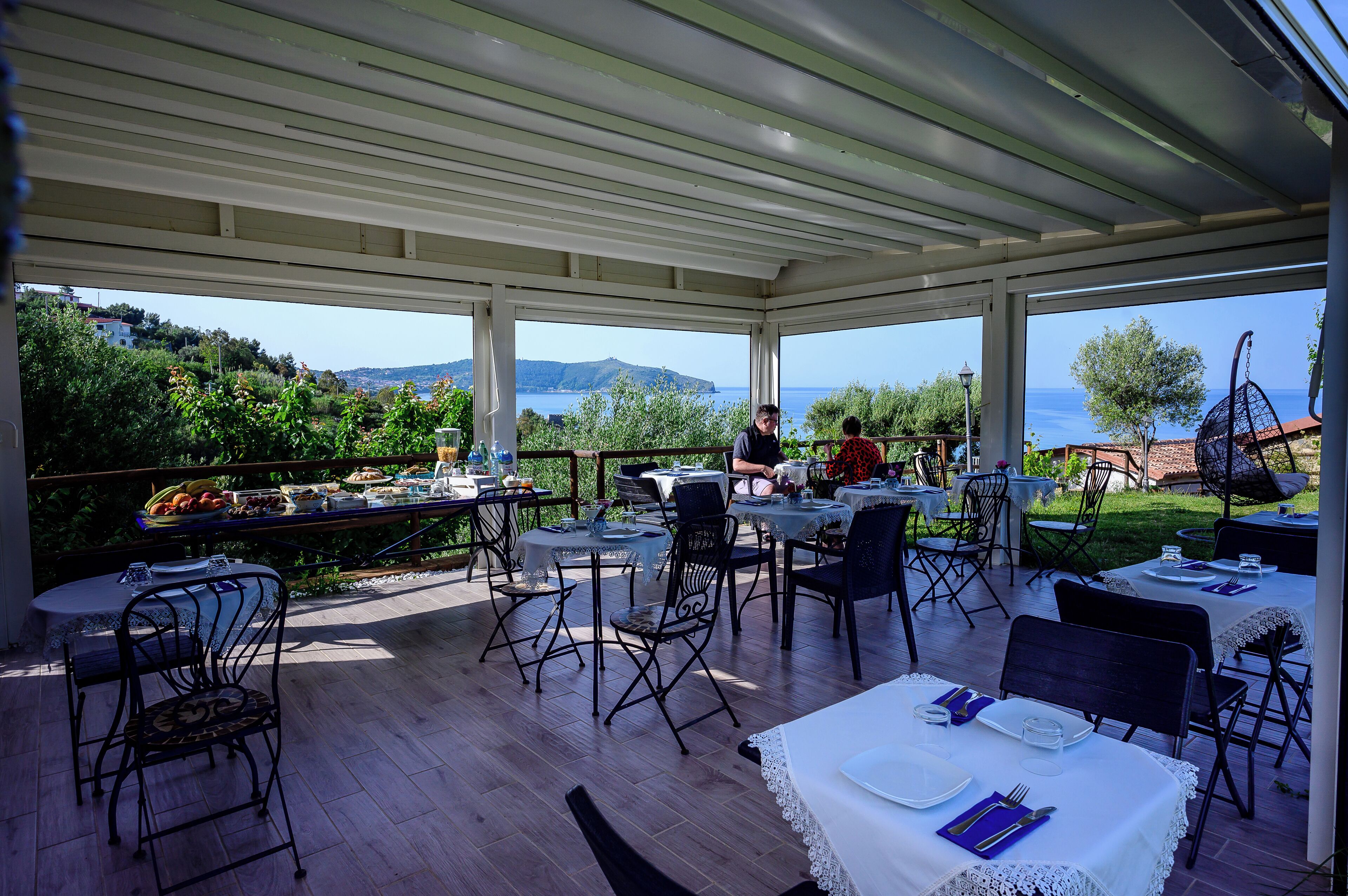 Un'area pranzo all'aperto con tavoli e sedie, con vista panoramica sul mare e sulle colline.