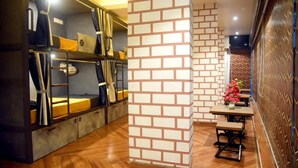 Une pièce chaleureuse avec des lits superposés, un mur décoratif en briques et un coin repas avec des tables et des chaises en bois.