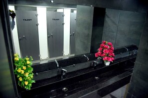 Eine öffentliche Toilette mit mehreren Kabinen, einem schwarzen Marmorwaschbecken und einem Blumentopf mit gelben Blüten.