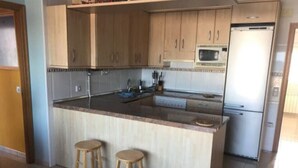 A kitchen with wooden cabinets, a microwave, a refrigerator, and two stools. - Fake penthouse with sea views and a large terrace (Llançà)
