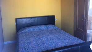 A single bed with a patterned bedspread in a room with yellow walls and a wooden door. - Fake penthouse with sea views and a large terrace (Llançà)
