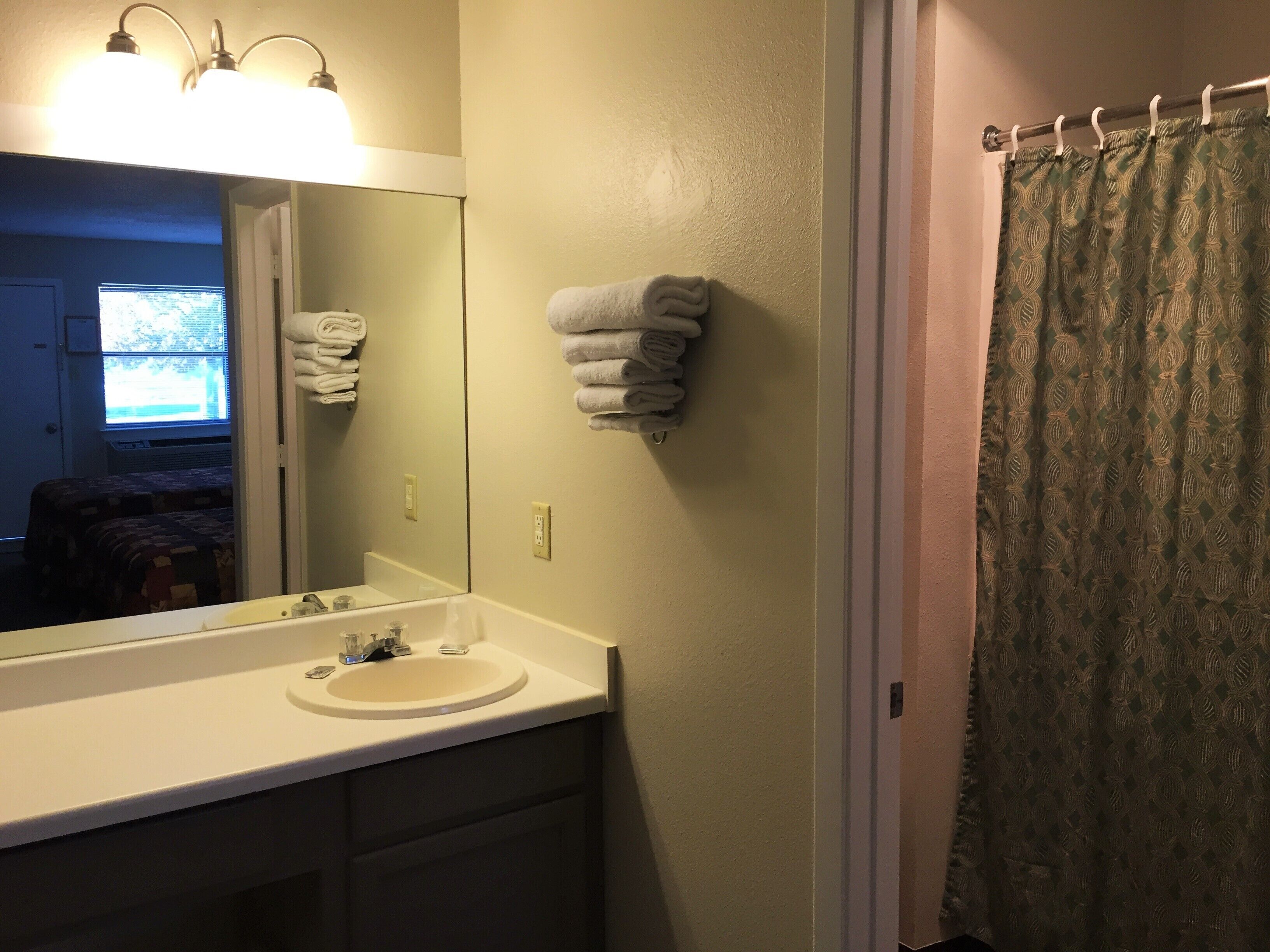 A bathroom with a sink, mirror, towel rack, and shower curtain.