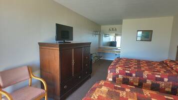 A bedroom with a bed, a wooden dresser, a television, a chair, and a bathroom with a sink and mirror.