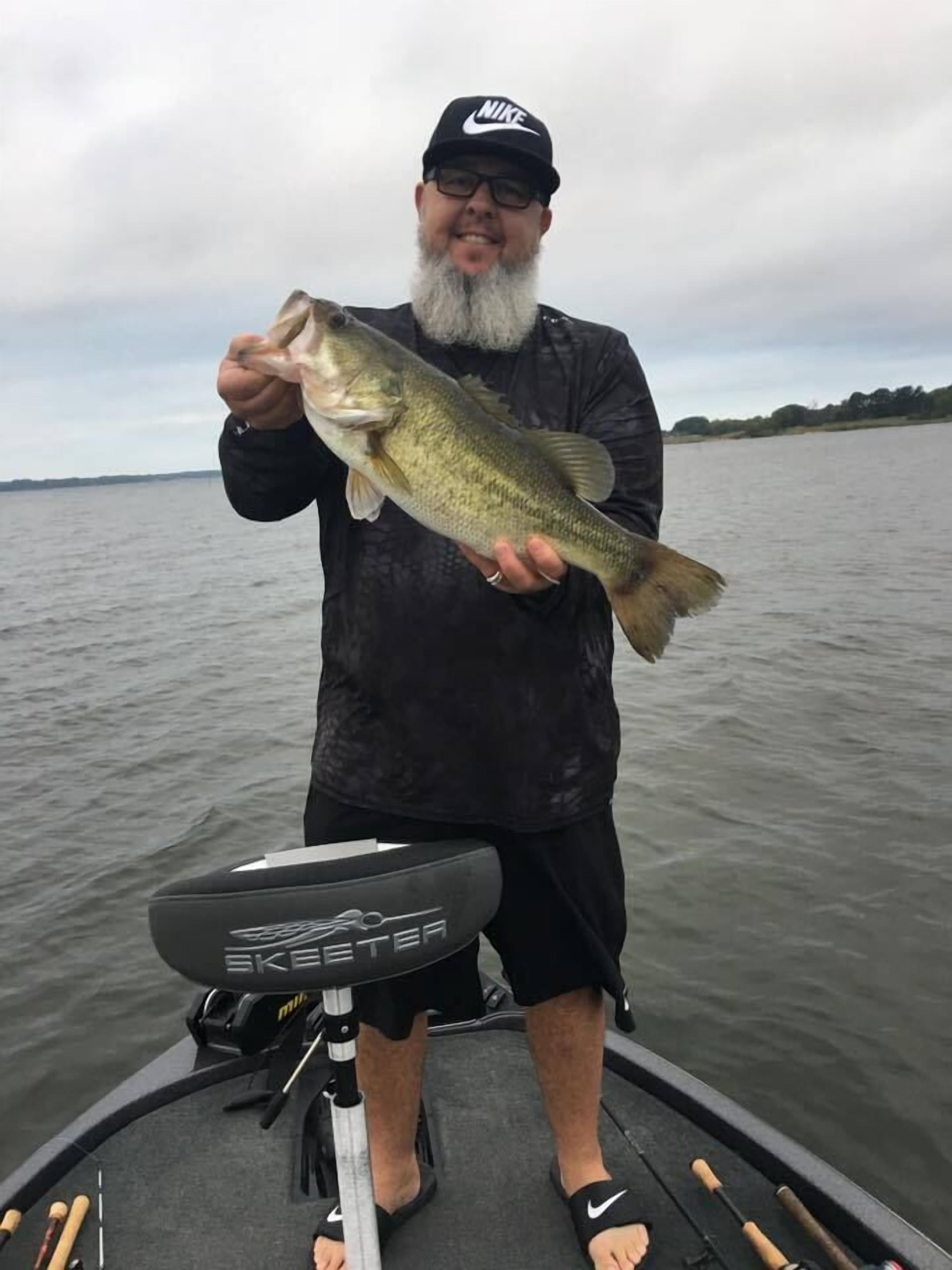 A person holding a fish on a boat with a fishing rod and a water skimmer.