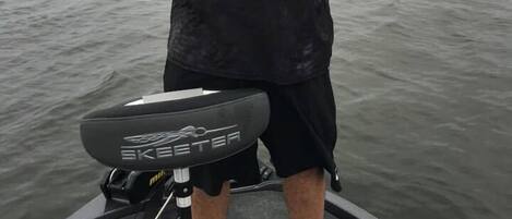 A person holding a fish on a boat with a fishing rod and a water skimmer.