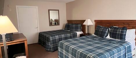 A hotel room with two beds, a desk, a chair, a lamp, a mirror, and a door.