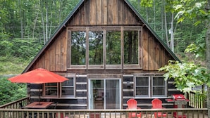 A log cabin with a deck, outdoor seating, and a grill.