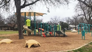 Ein Spielplatz mit Rutsche, Klettergerüsten und einem schattigen Bereich.