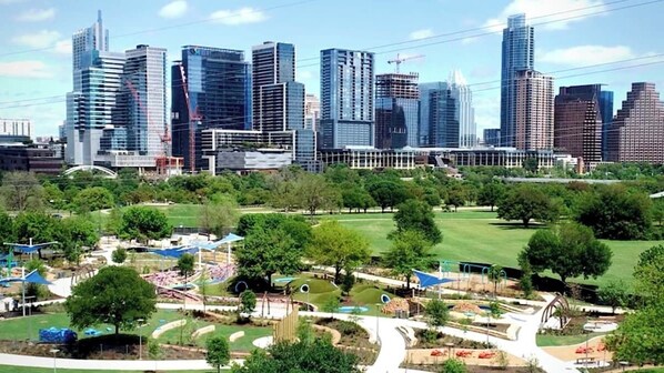 Un paisaje urbano con rascacielos modernos y un parque con juegos infantiles y senderos peatonales.