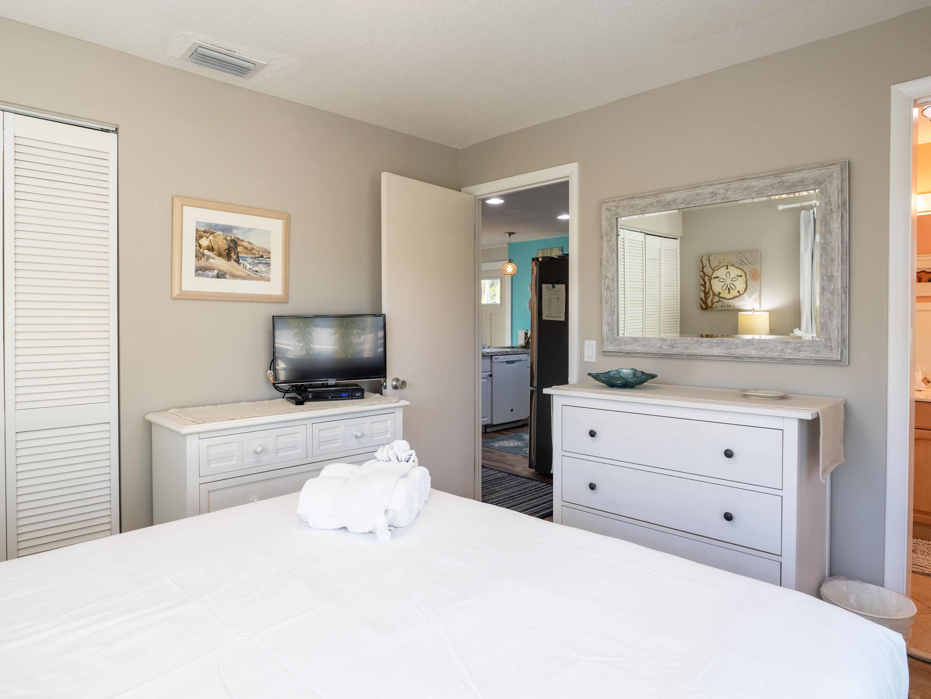 A hotel room with a bed, a television, a dresser, and a mirror.