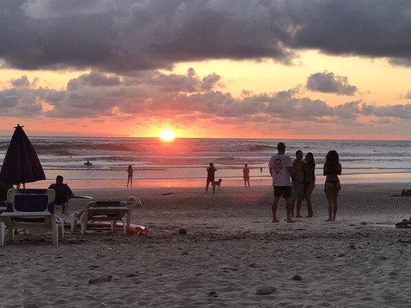 Une scène de plage avec des gens, un coucher de soleil et une mer calme.