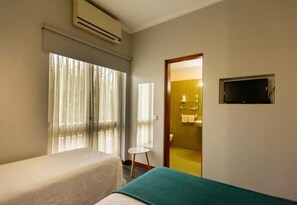 Une chambre d’hôtel avec deux lits, une télévision et une salle de bain visible à travers une porte ouverte.