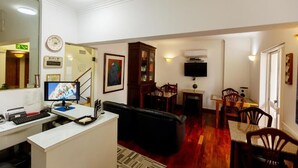 A living room with a desk, computer, and a television. There is a dining area with chairs and a table. - Hotel São Nicolau (Braga)