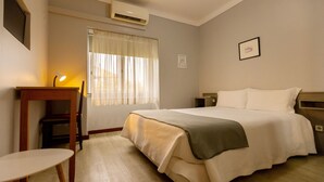 A hotel room with a bed, bedside table, lamp, and a window with curtains. - Hotel São Nicolau (Braga)