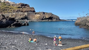 Ein felsiger Strand mit badenden und sonnenbächelnden Personen.