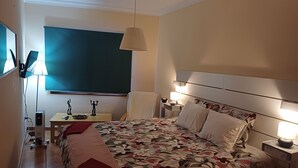 Ein Hotelzimmer mit Bett, Nachttischen, einem Schreibtisch mit Lampe, einem Sessel und einem großen Fenster mit Blick.