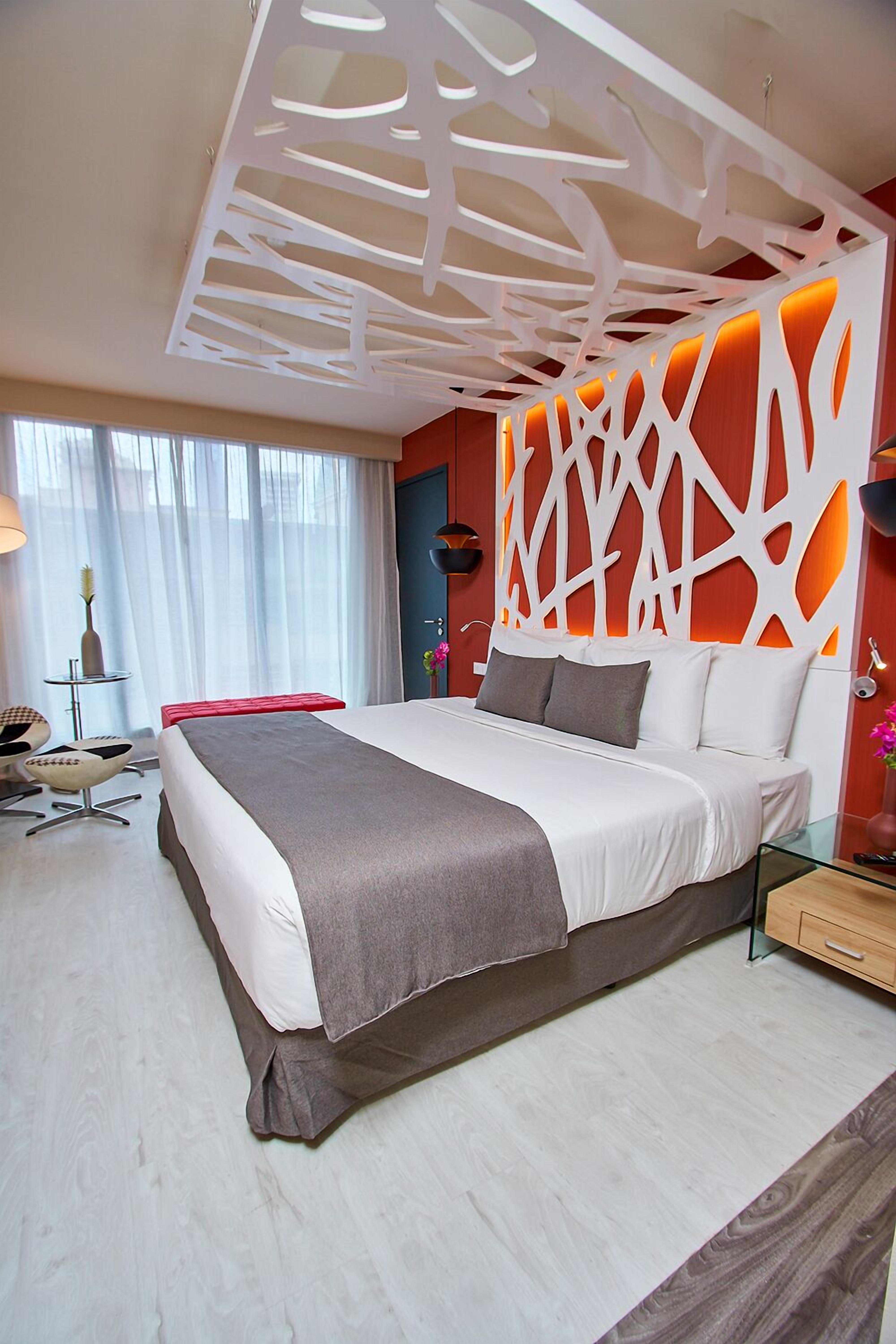 Une chambre d’hôtel moderne avec un grand lit, une table de chevet en verre et un panneau décoratif mural.