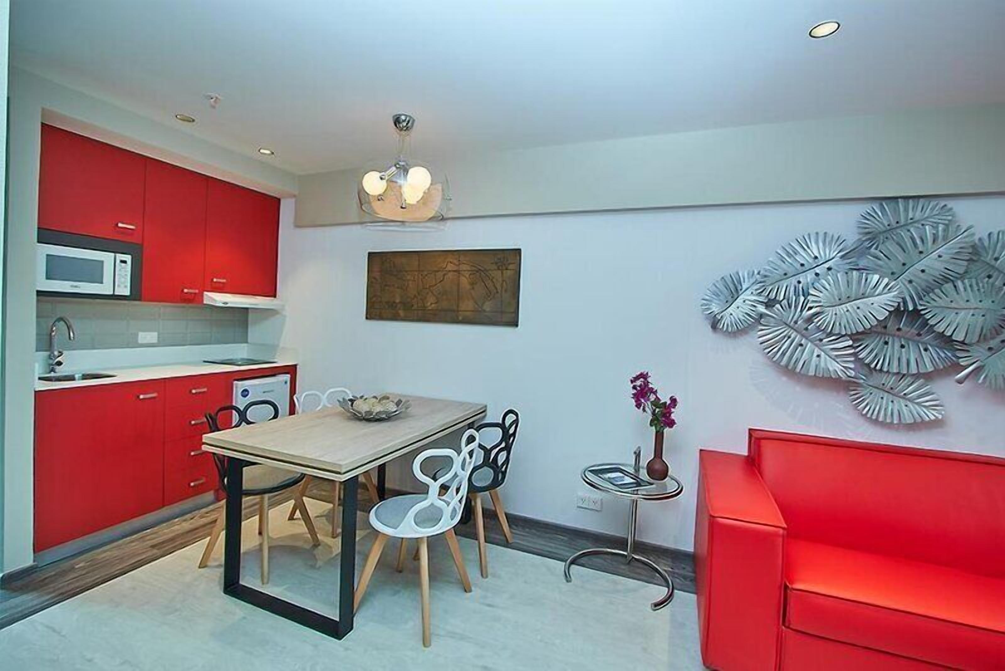A modern kitchen with red cabinets, a dining table with chairs, a microwave, and a ceiling light fixture.