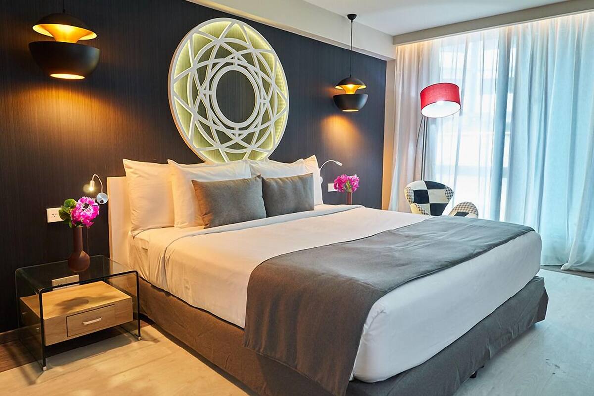 Une chambre d’hôtel moderne avec un grand lit, un élément décoratif mural et deux lampes suspendues.
