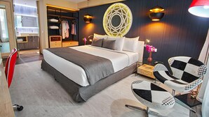 Una habitación de hotel moderna con una cama grande, un armario, un escritorio con silla y un elemento decorativo en la pared.