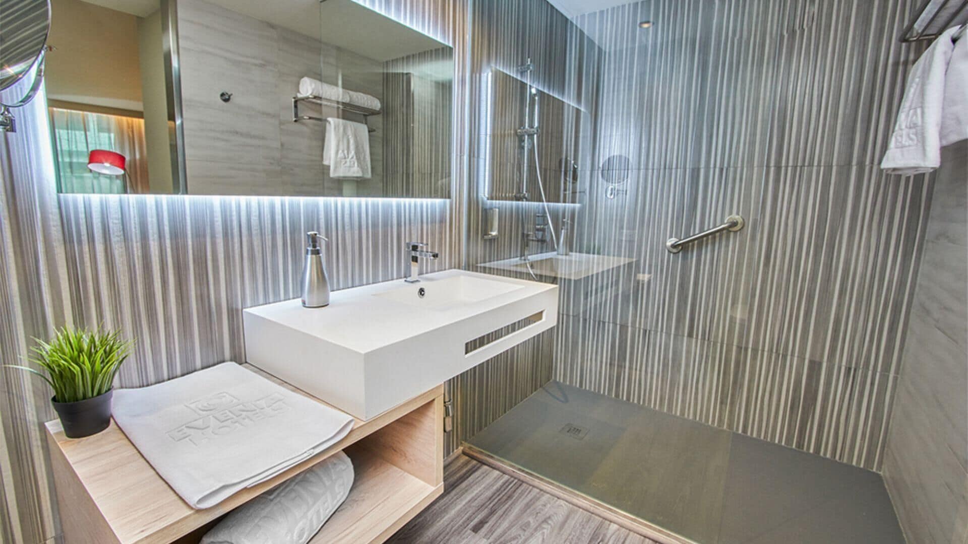 Een moderne badkamer met een douchecabine van glas, een wit wastafeltje en een handdoekhouder.