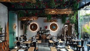 Un restaurante con mesas y sillas de madera, plantas colgantes y decoraciones circulares en la pared.