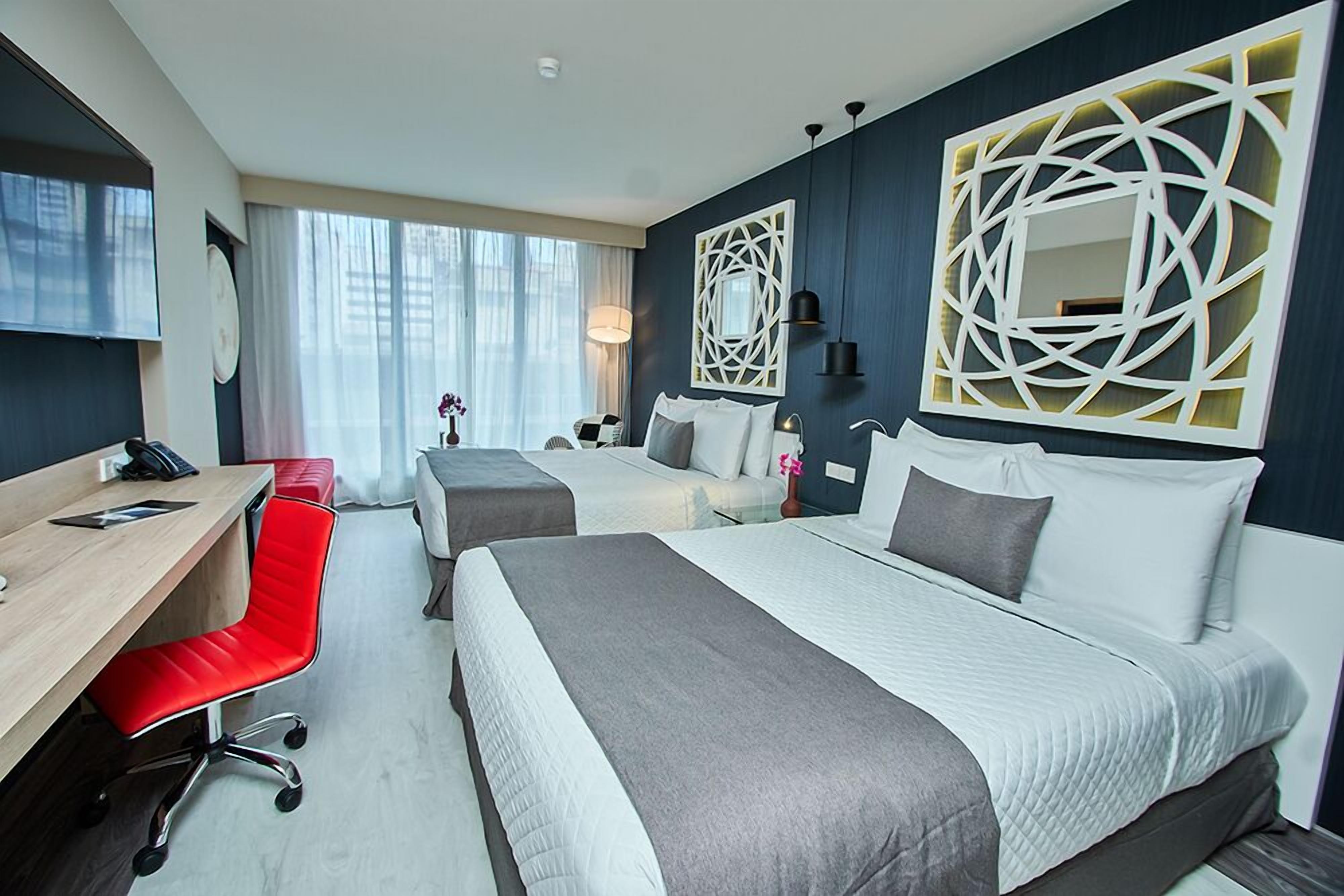A hotel room with two beds, a desk, and a red chair.