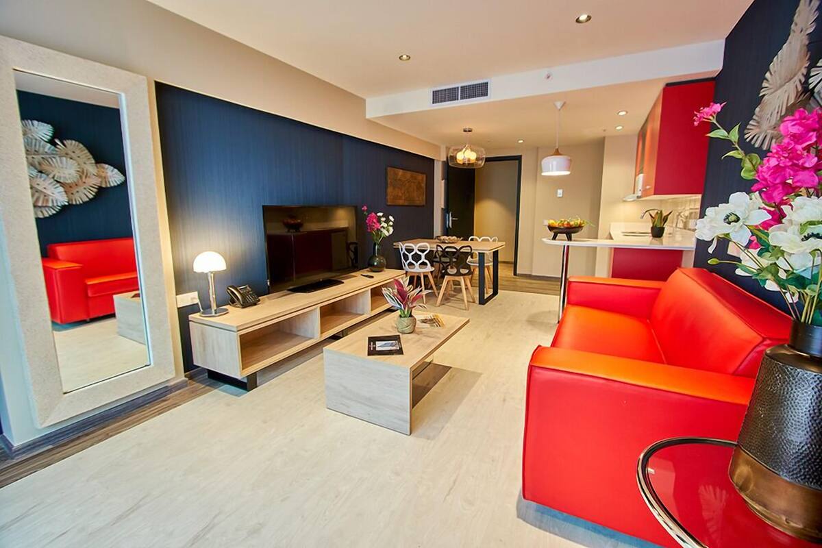 Un salon moderne avec un canapé rouge, un téléviseur, un coin repas et une cuisine en arrière-plan.