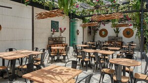 Un café al aire libre con varias mesas y sillas de madera, rodeado de follaje y detalles decorativos.