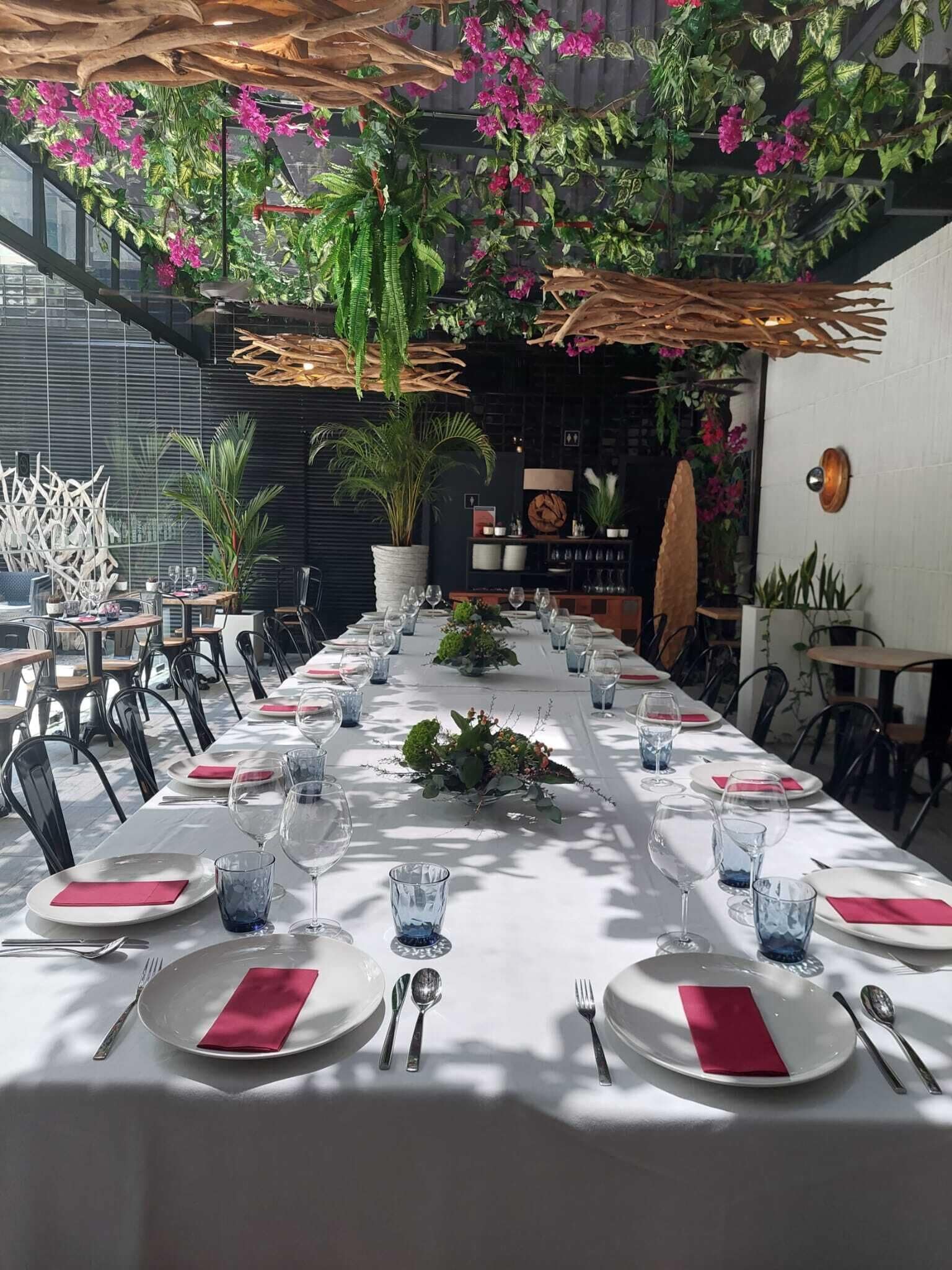 Una larga mesa de comedor vestida con manteles blancos, servilletas rojas y copas de cristal, rodeada de sillas.
