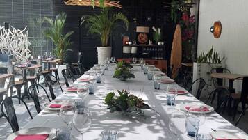 Una larga mesa de comedor vestida con manteles blancos, servilletas rojas y copas de cristal, rodeada de sillas.