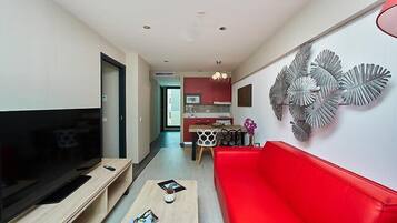 Een moderne woonkamer met een flatscreen televisie, een rode bank, een salontafel en een eethoek met een keuken op de achtergrond.