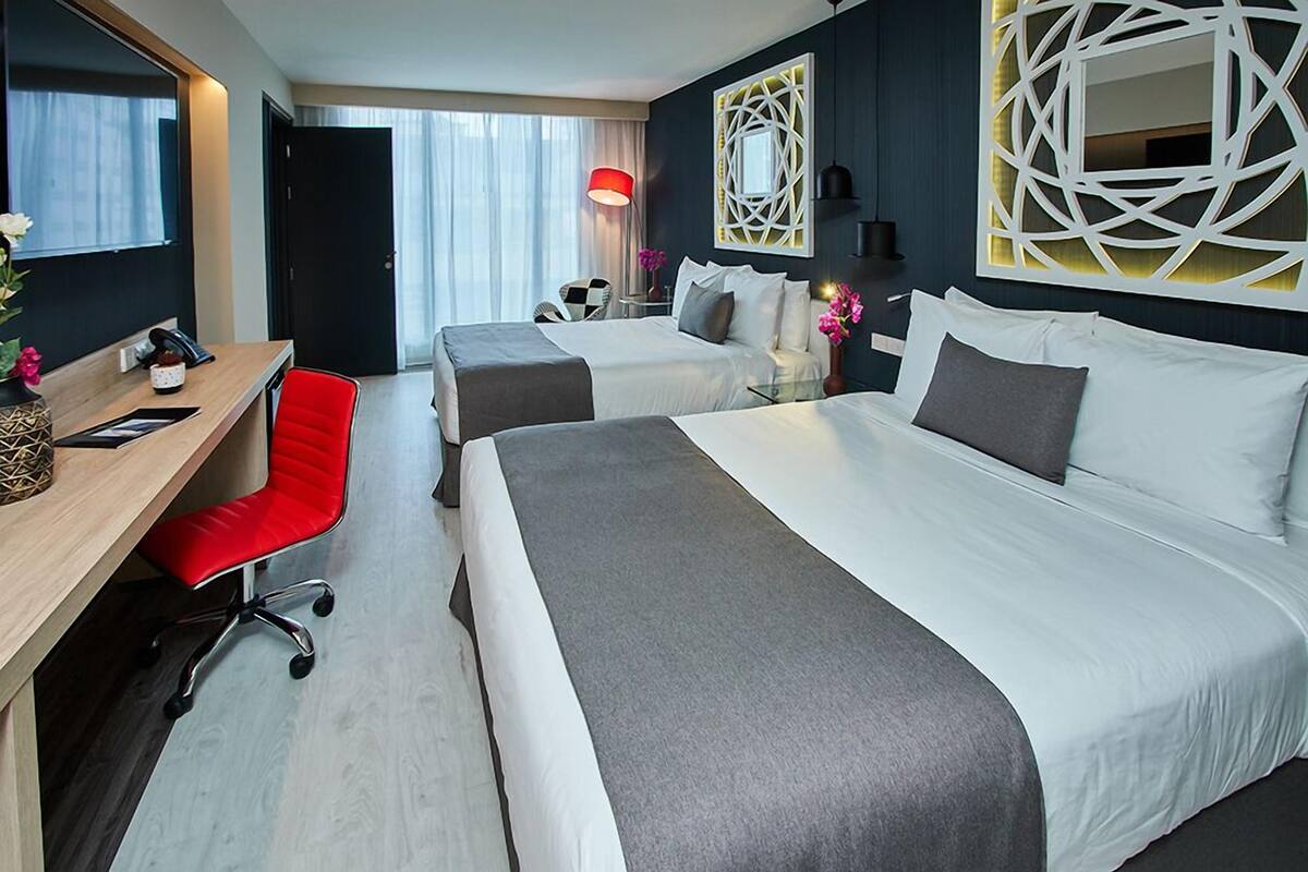 Une chambre d’hôtel avec deux lits, un bureau, une chaise rouge, une lampe et un élément décoratif mural.