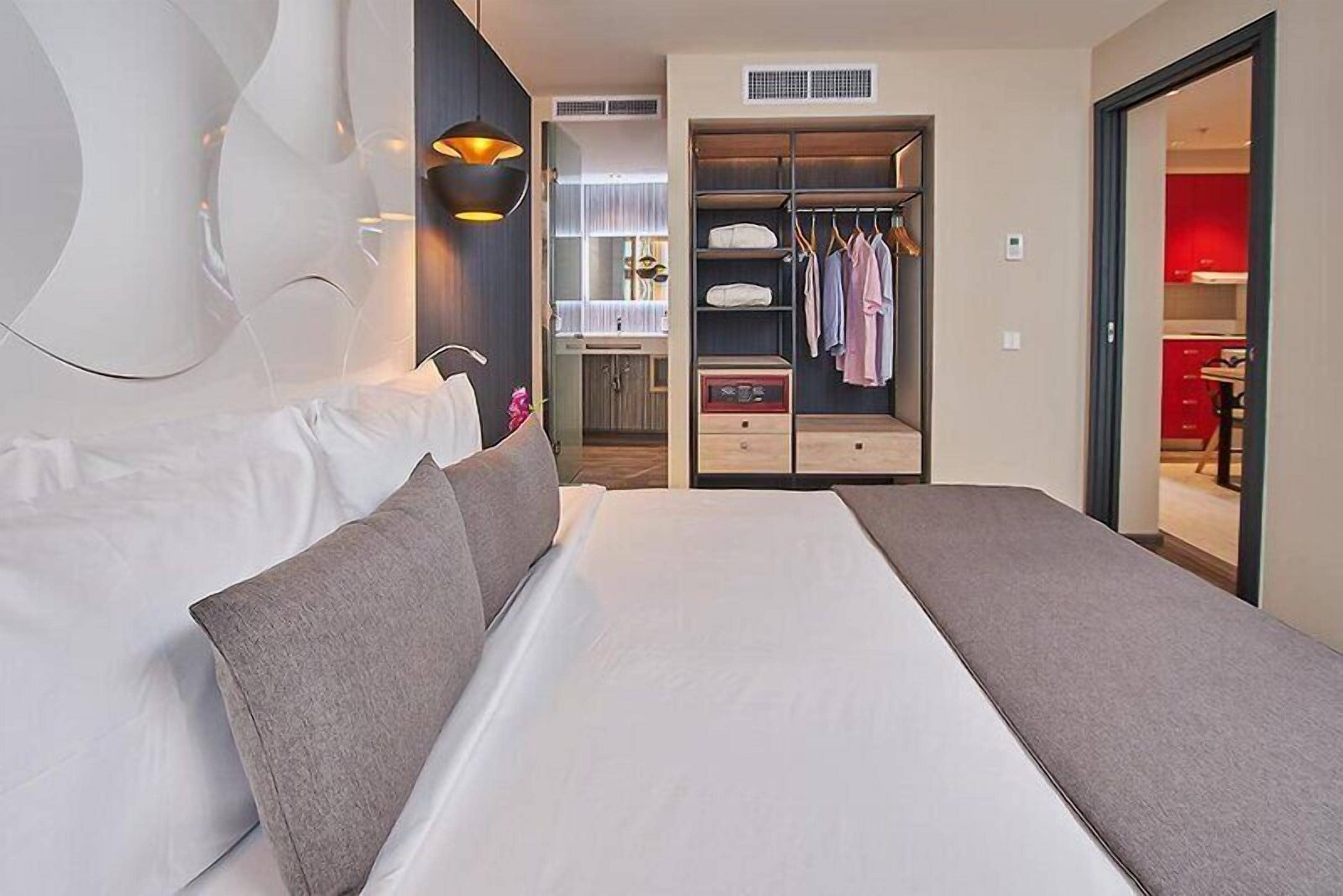 A modern hotel room with a large bed, a walk-in closet, and a view of the kitchen.