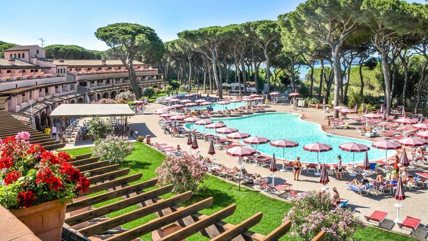Un complexe hôtelier doté d’une grande piscine entourée de transats et de parasols, d’un patio couvert et d’un bâtiment avec un toit en tuiles de terre cuite.