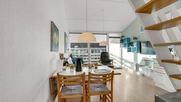 Et moderne spiseområde med et træbord og stole, et stort vindue med naturligt lys og en trappe med et geometrisk design.