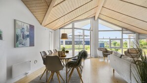 A spacious room with a high ceiling, a dining area with a table and chairs, a sofa, and large windows offering a view of the outdoors. - 3 bedroom lovely home in Jægerspris (Jægerspris)