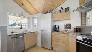 A modern kitchen with wooden ceiling beams, stainless steel appliances, and a view of a house through the window. - 3 bedroom lovely home in Jægerspris (Jægerspris)