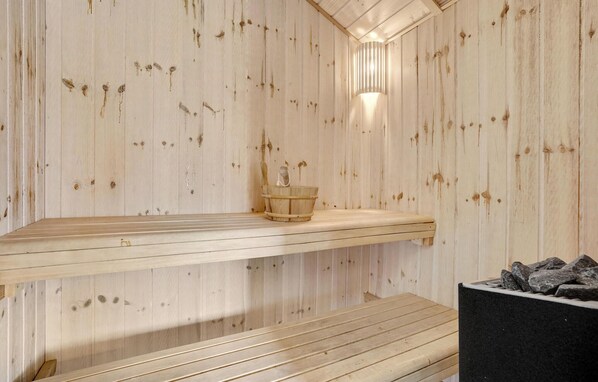 Eine Sauna mit Holzwänden, einer Bank, einem Eimer und Ablageflächen aus Stein.