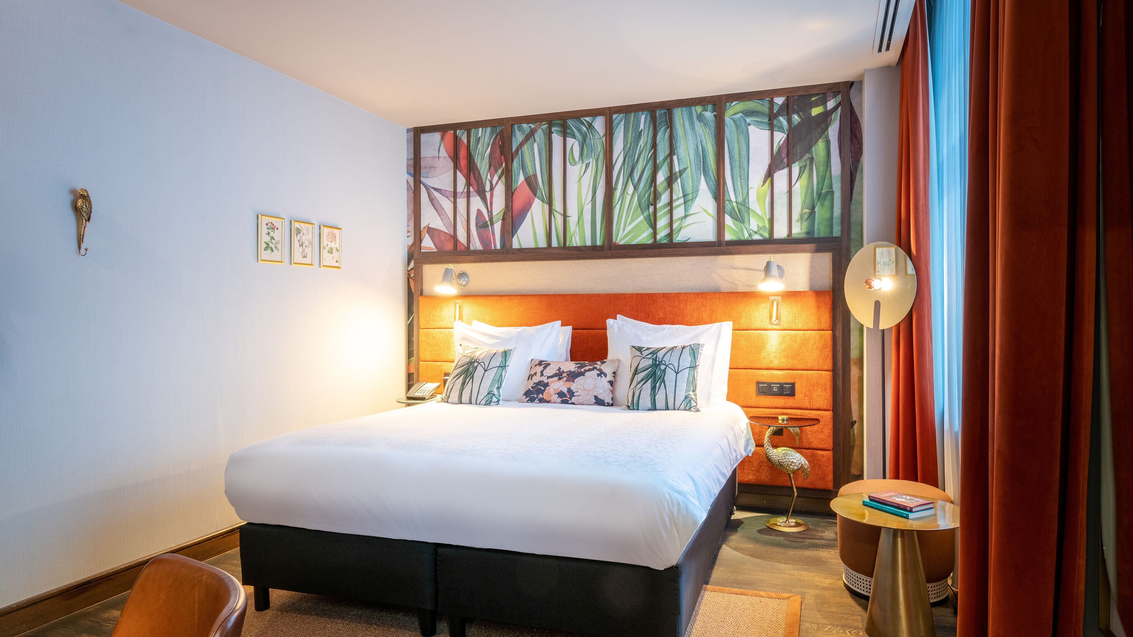A hotel room with a large bed, a nightstand, a small table, and a wall-mounted lamp.