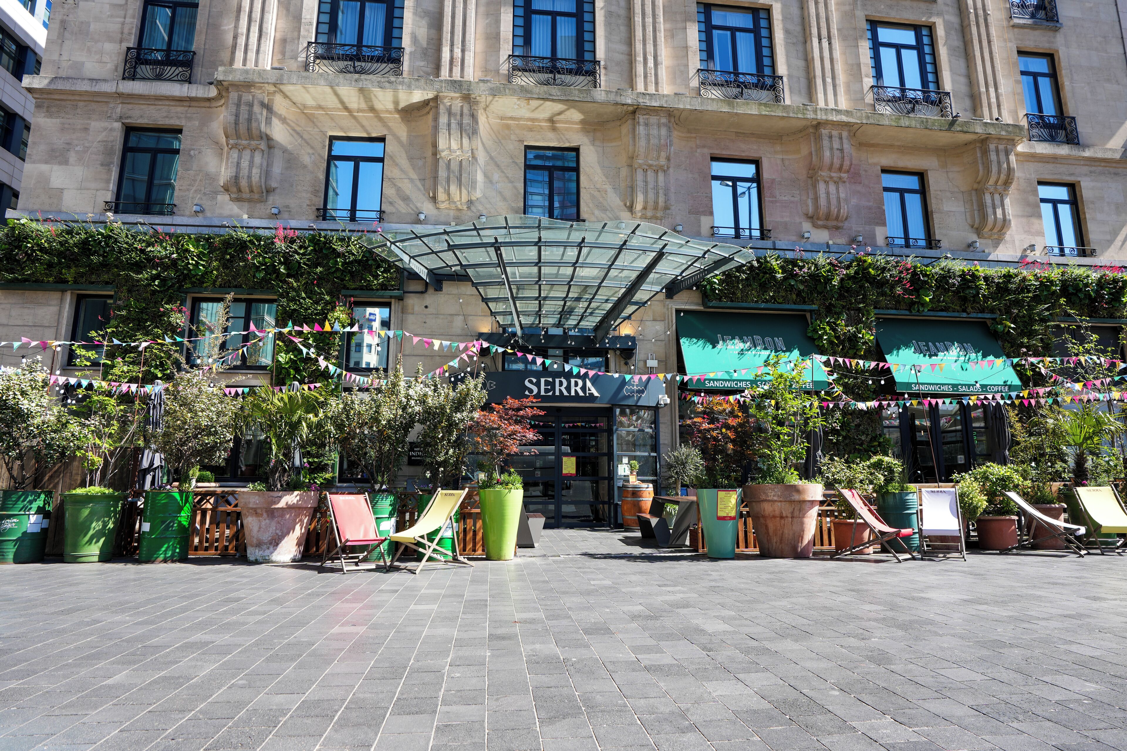 A hotel entrance with a covered entrance, outdoor seating area with chairs, and potted plants.