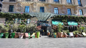 A hotel entrance with a covered entrance, outdoor seating area with chairs, and potted plants.