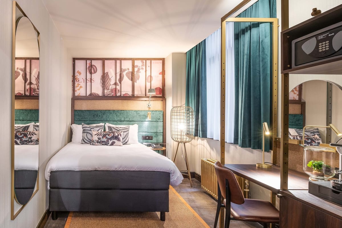A hotel room with a bed, desk, chair, and a large mirror.