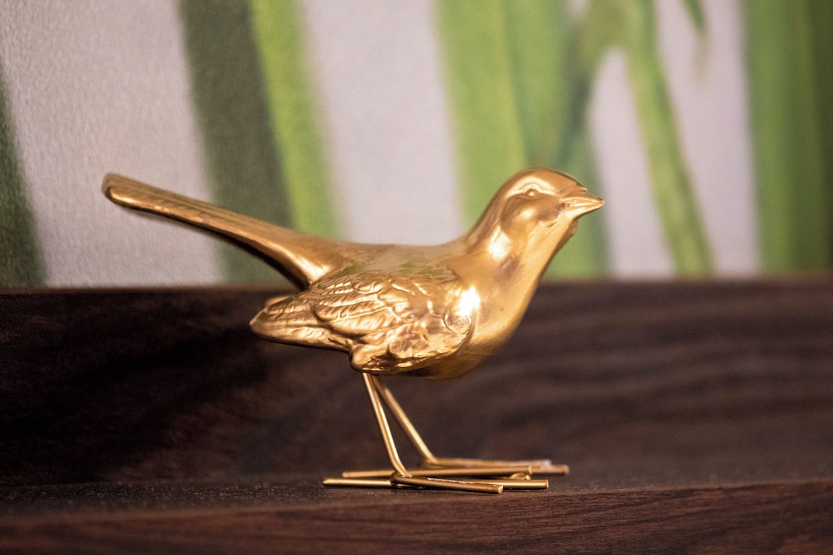 A golden bird figurine on a wooden stand.